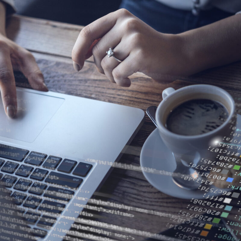 Aparece una mesa, donde hay un ordenador, un cafe, un móvil y se ve como dos manos de mujer escriben en el teclado del ordenador.